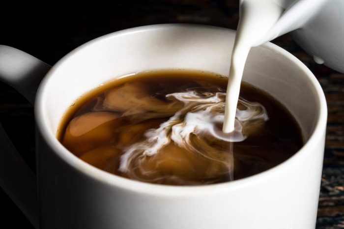 Pouring cream into a cup of coffee