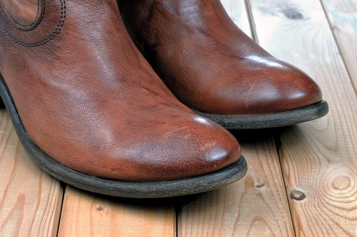 Pair of new classic leather brown cowboy boots on wooden boards. Macro shooting