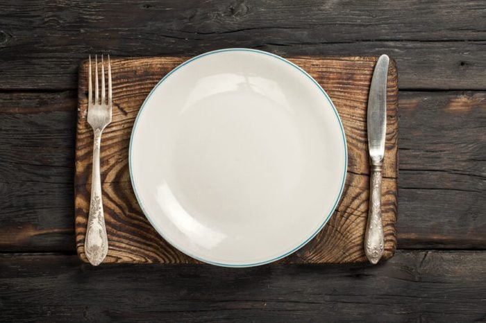 White empty plate with fork and knife on a old wooden board on a dark wooden background, top view