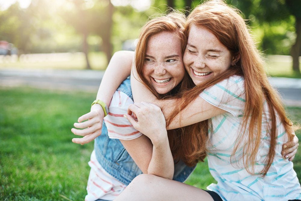 Young girl hugging her older sister smiling. Two red haired ladies having the best time of their lives.