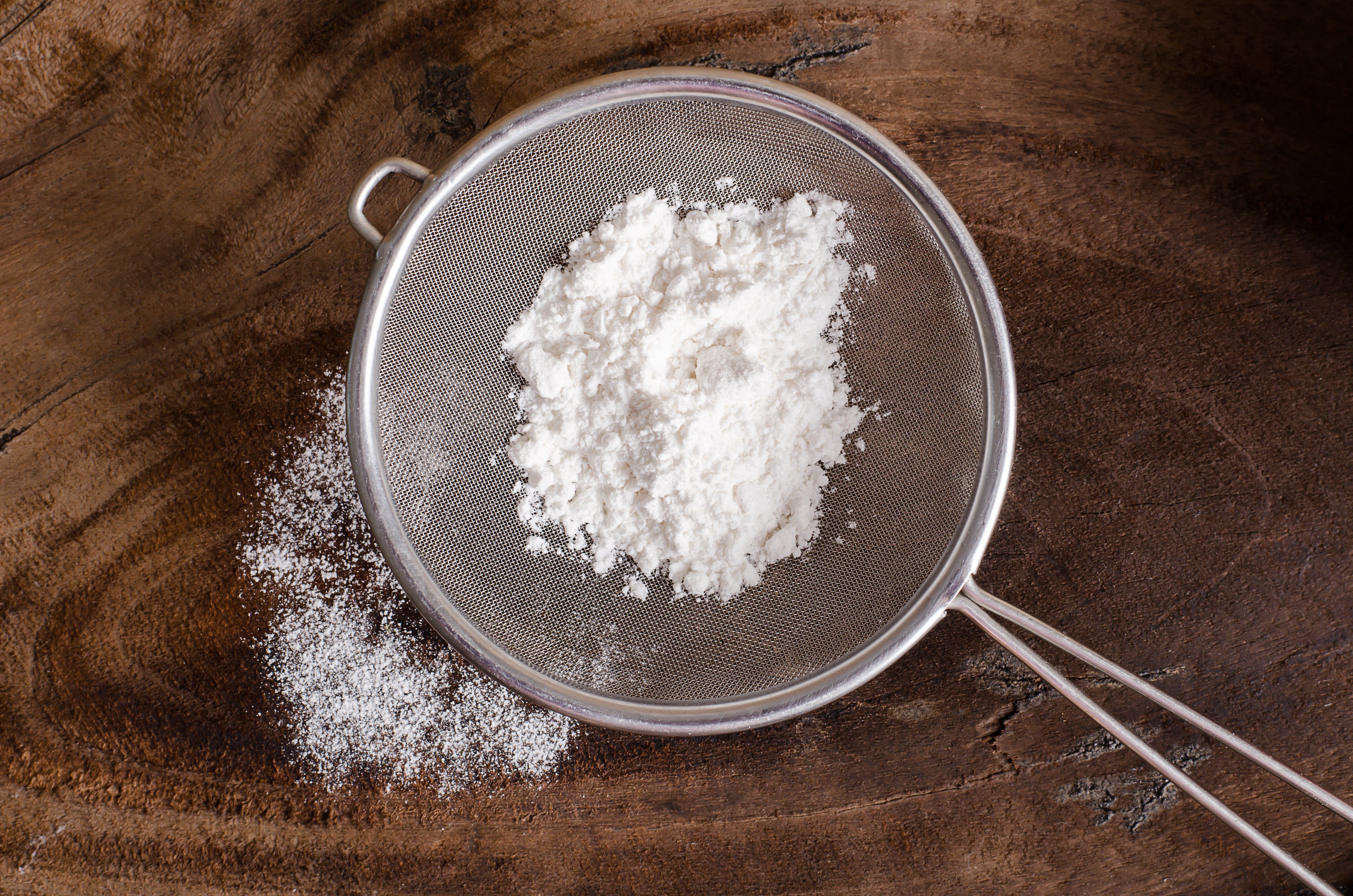 Wheat flour in a sieve on wooden background, food ingredient, prepare for cooking or baking