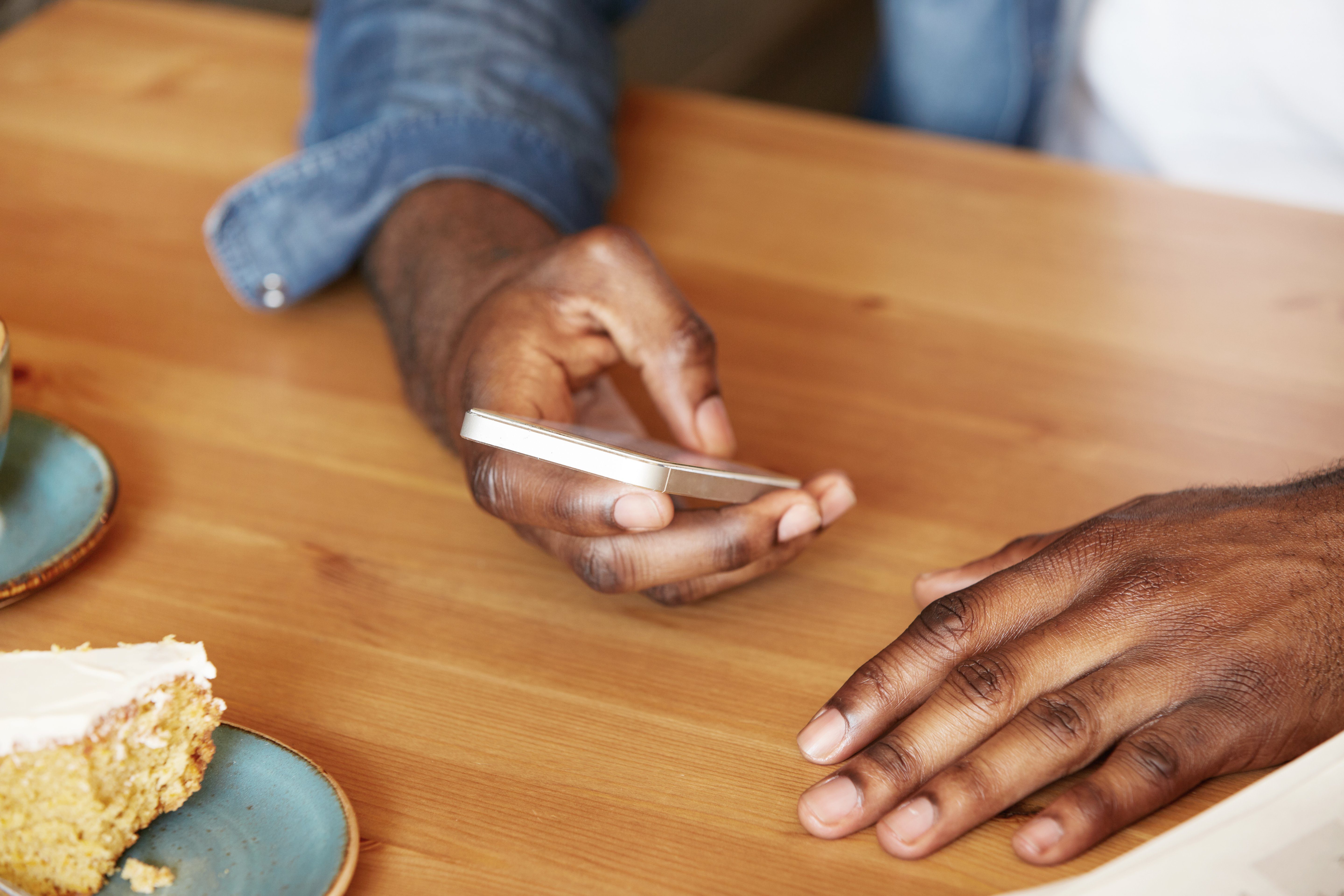 Film effect. Close up shot of African man's hands holding mobile phone while using wireless high-speed Internet connection. Black student texting friends via social networks sitting at a coffee shop