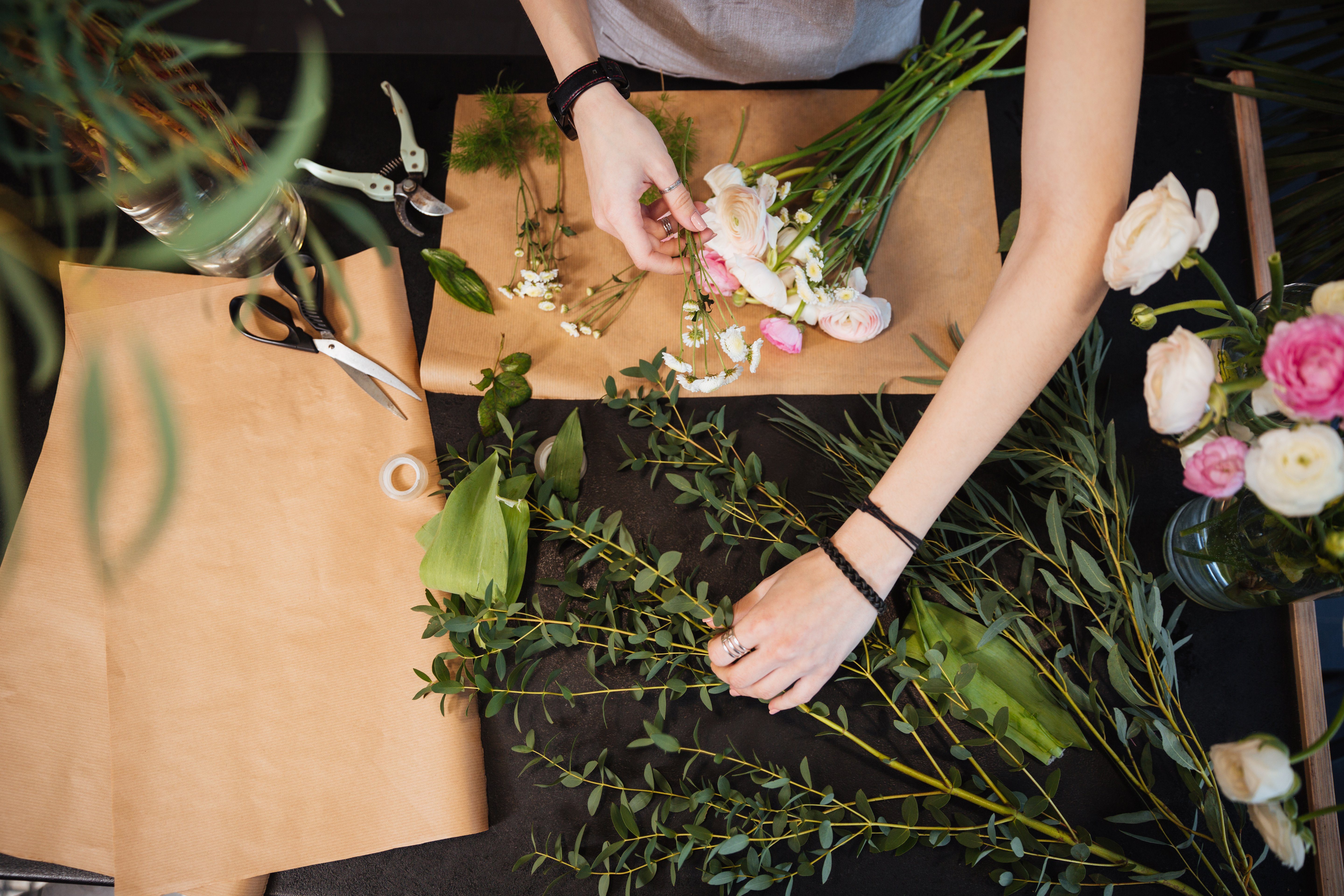 Top view of hands of young woman florist creating bouquet of flowers on black table