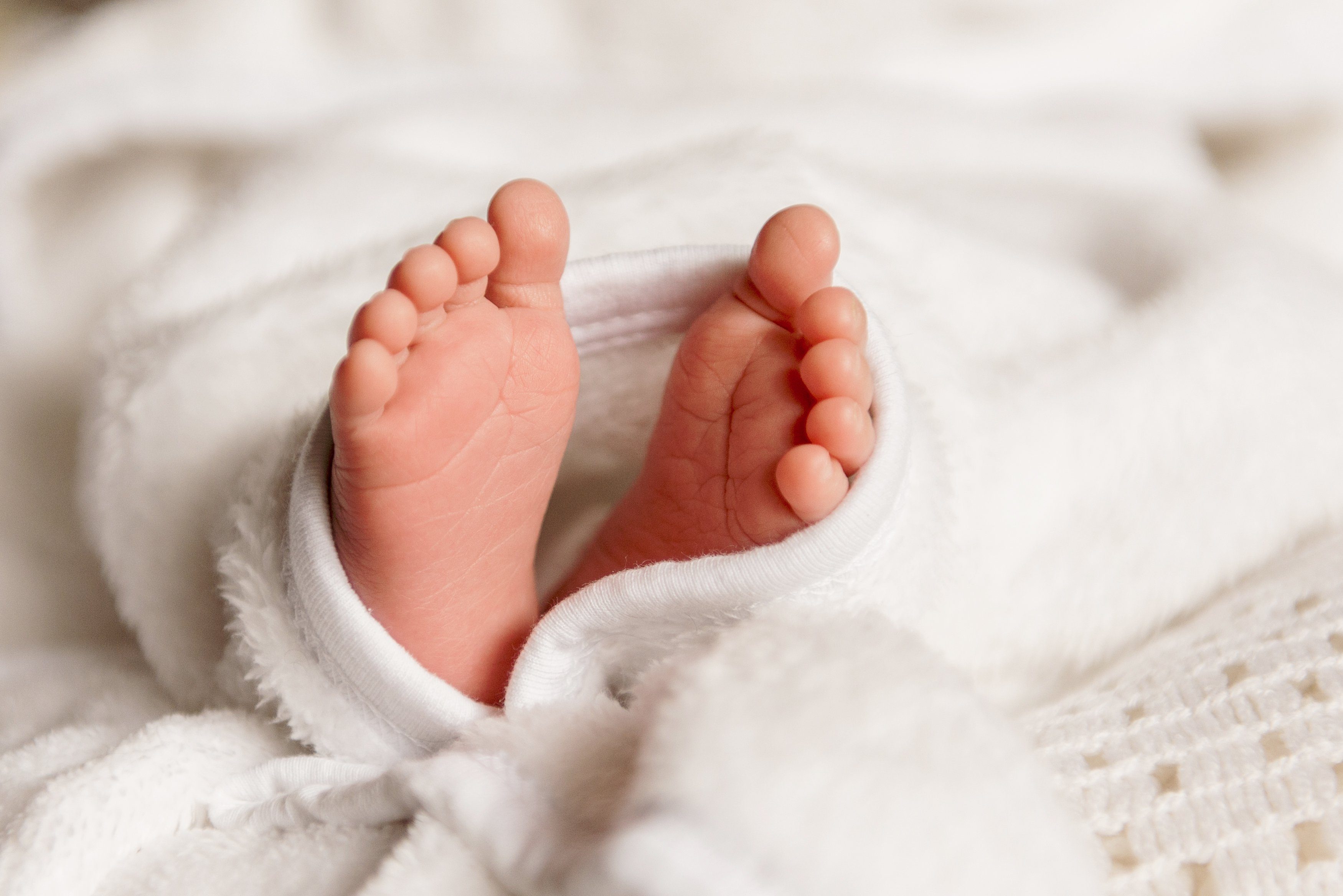 Bare feet of a cute newborn baby in warm white blanket. Childhood. Small bare feet of a little baby girl or boy. Sleeping newborn child.