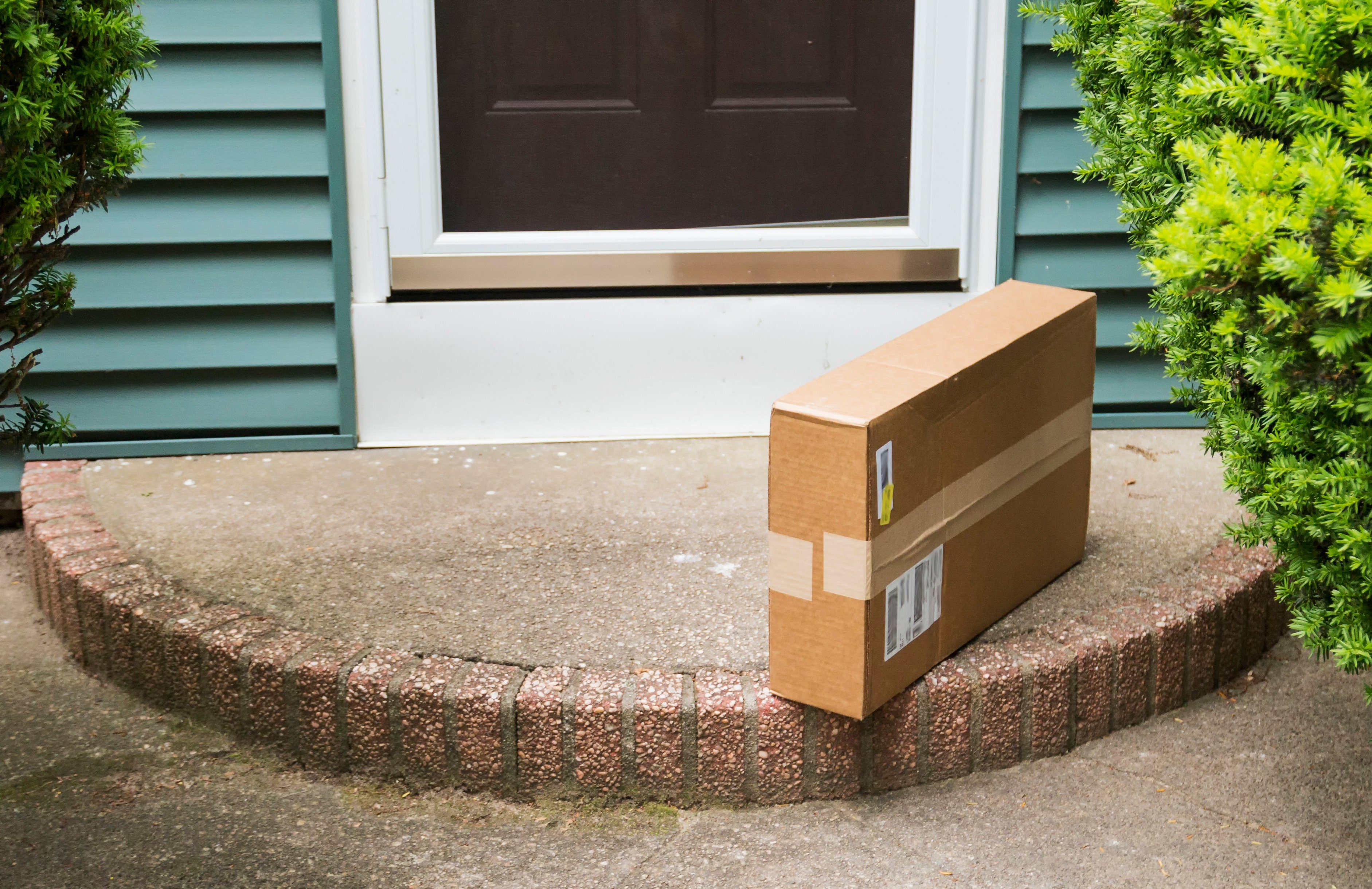 A brown cardboard box is left on the front stoop after being delivered while no one was home.