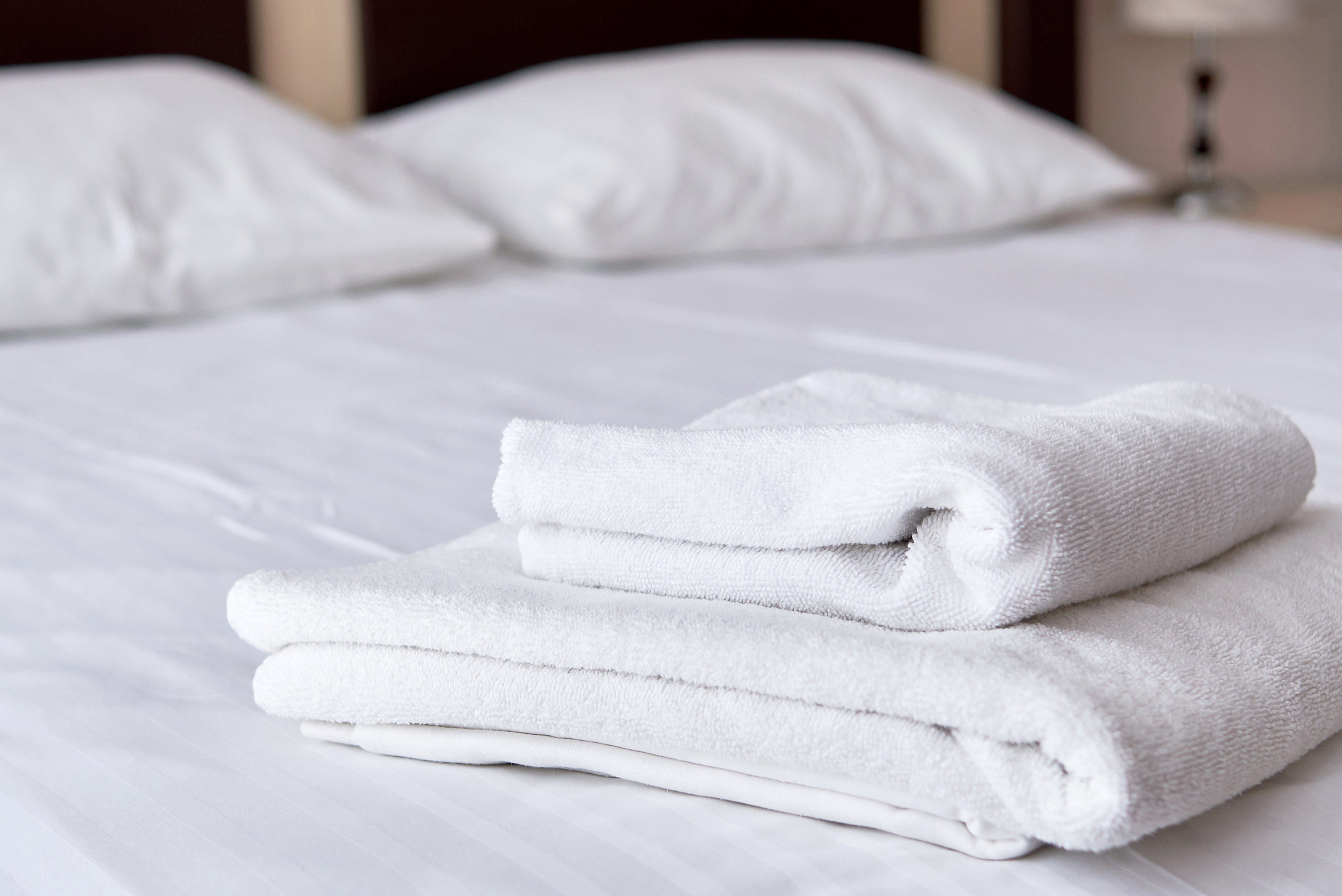 Close up of stack of white clean bath towels on bed sheet in modern hotel bedroom interior, copy space