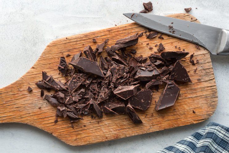 Прерванный темный шоколад на кухонной доске.  Вид сверху.