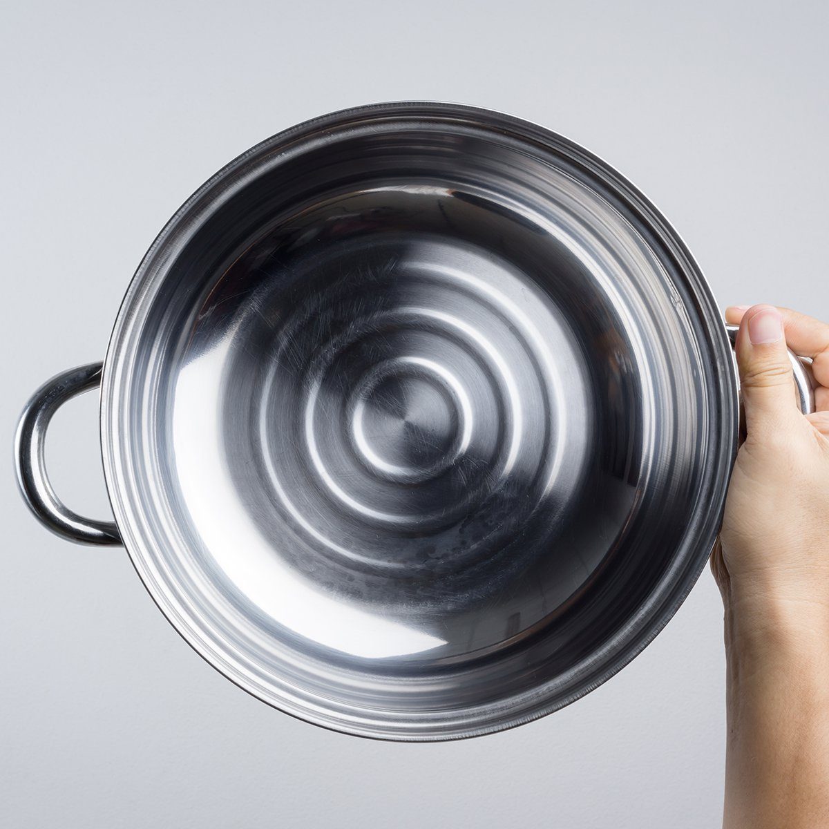 Hand holding stainless steel pan or wide pot on white background