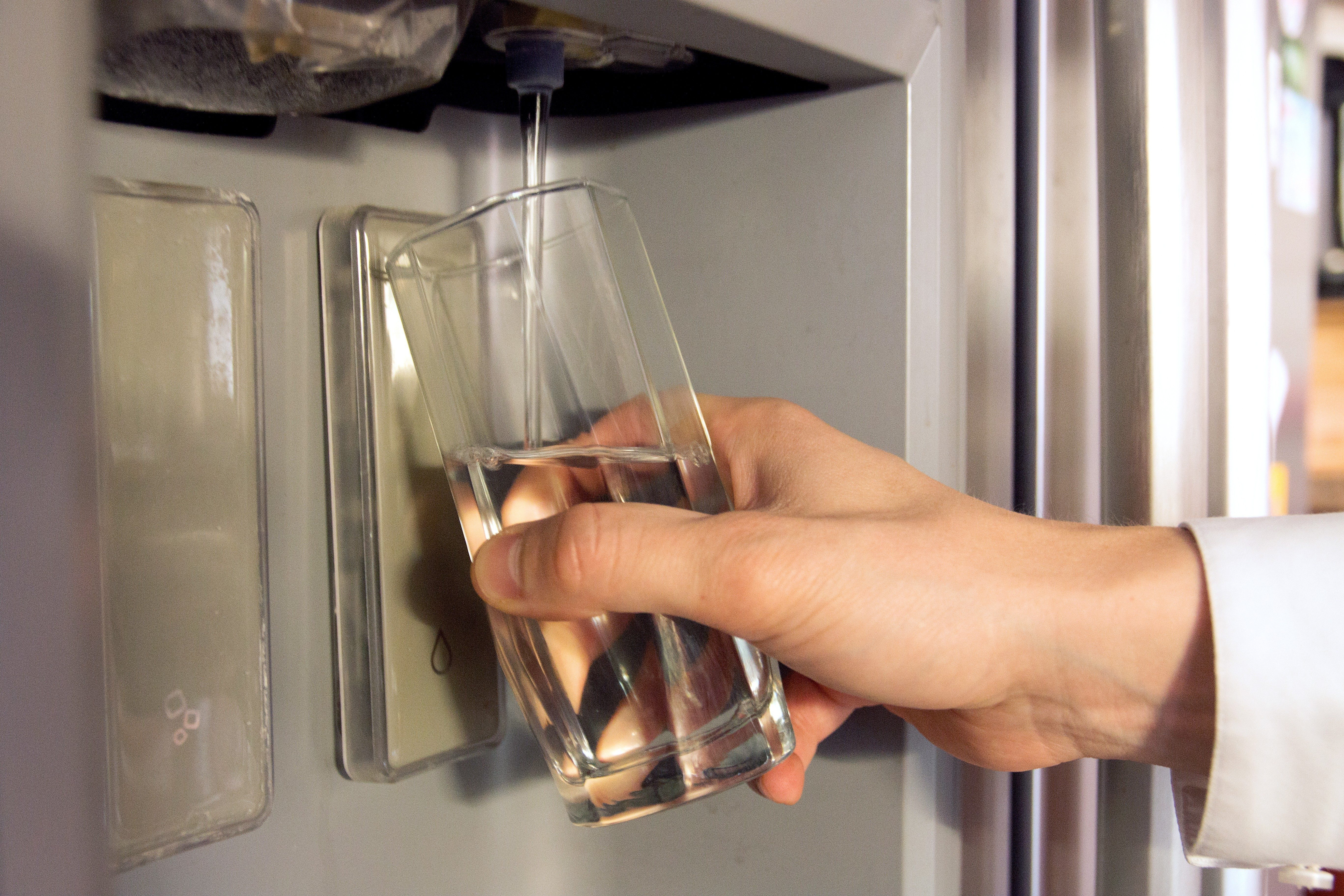 Male hand is pouring cold water from dispenser of home fridge.