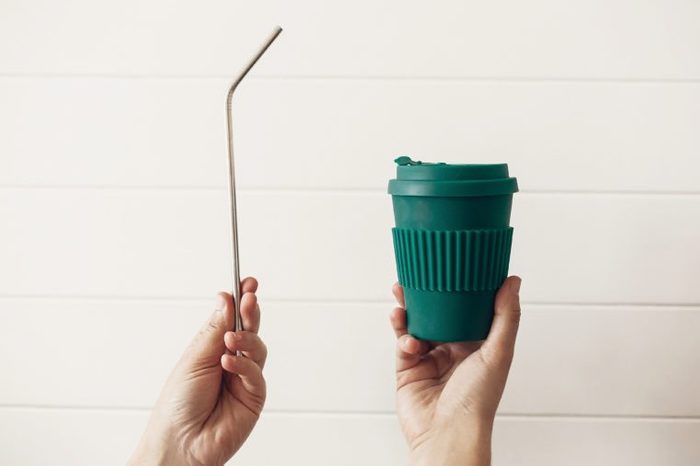 Hands holding stylish reusable eco coffee cup and steel straw on white wooden background. Zero waste. Green Cup from natural bamboo fiber and metallic straw, Ban single use plastic.