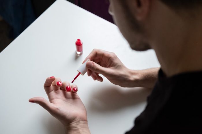 Man with a beard making manicure for himself, holding red nail polish. Lifestyle photo. Lgbt community. Transsexual guy. 