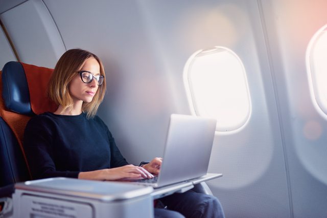 Traveling and technology. Flying at first class. Pretty young businees woman working on laptop computer while sitting in airplane.