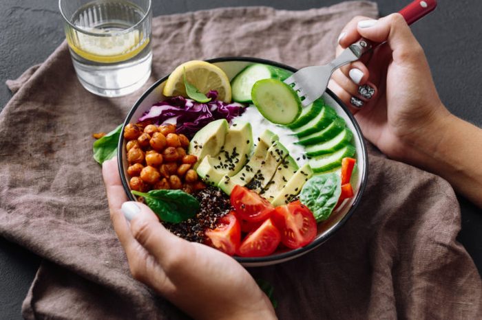 Woman is eating healthy lunch on dark background. Buddha bowl. Clean and balanced healthy food concept