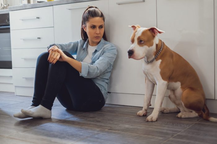 Woman sitting on the kitchen floor mad on her dog who is sad
