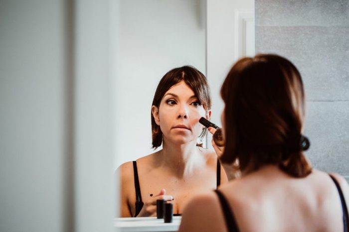 Young and pretty short-haired woman putting on makeup in front of the mirror in her house in the morning. Lifestyle.