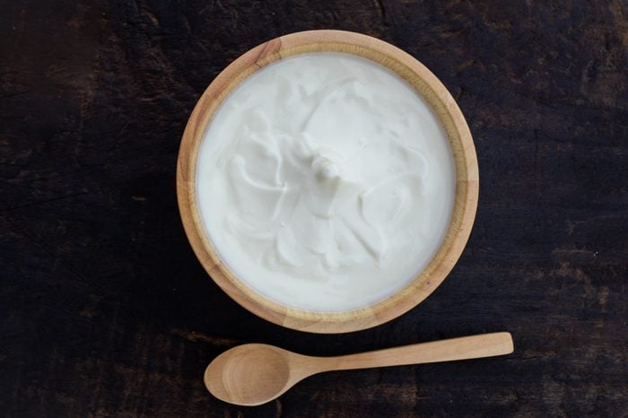 Greek yogurt or sour cream in a wooden bowl on dark table top view. Healthy food nutrition.