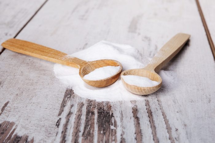 Baking soda on wooden spoon on white wooden textured background.