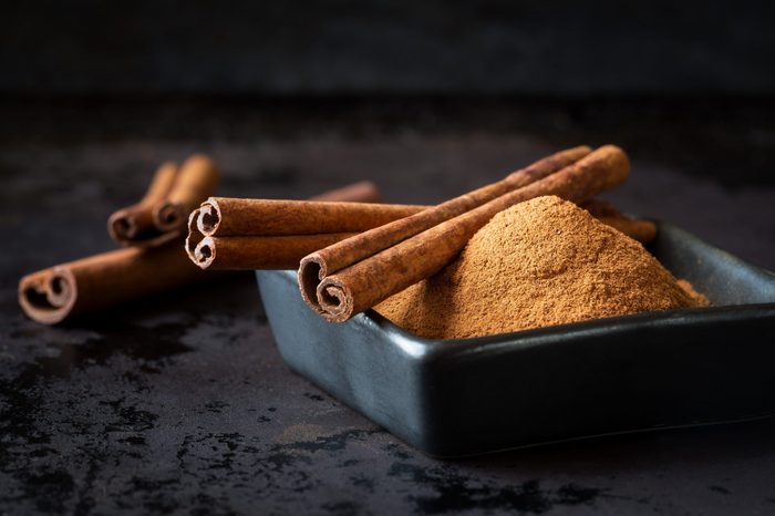 Ground cinnamon powder and cinnamon sticks in a black bowl on dark rustic background