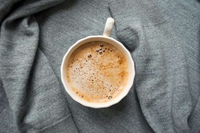 A cup of fresh coffee with beautiful foam on grey background. Flat lay style.