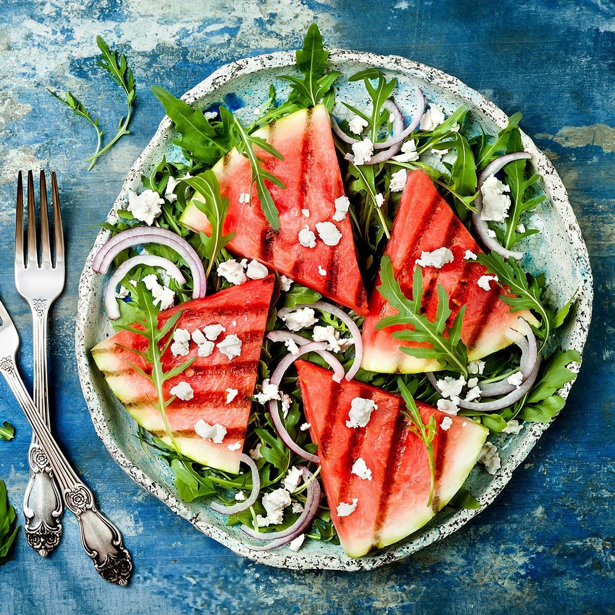 Fresh summer grilled watermelon salad with feta cheese, arugula, onions on blue background