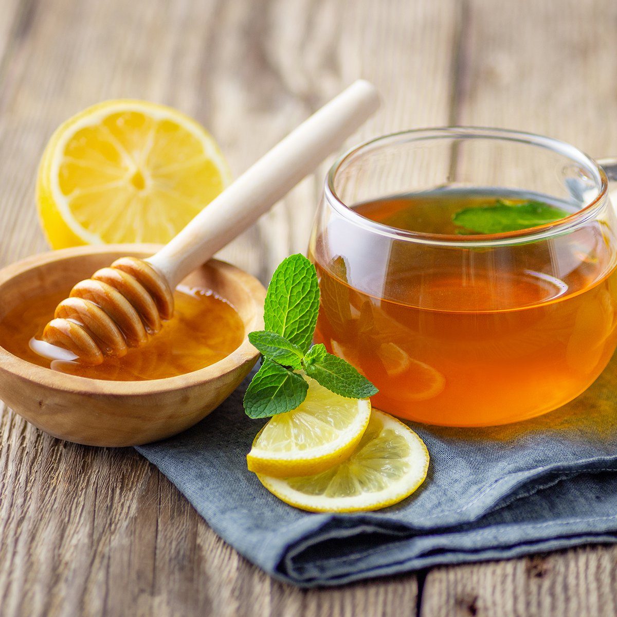 A glass cup of tea with lemon, mint, ginger and honey on wooden rustic table.