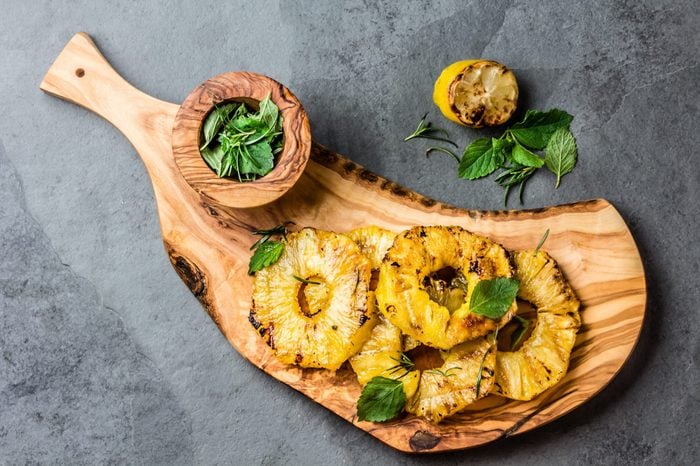 Grilled pineapple slices with mint on olive wooden board. top view