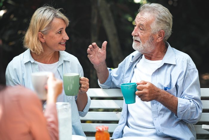 rude conversation habits - Family lunch outdoor. Couple of white and asian senior man and woman sitting and holding coffee cup other in tropical garden.