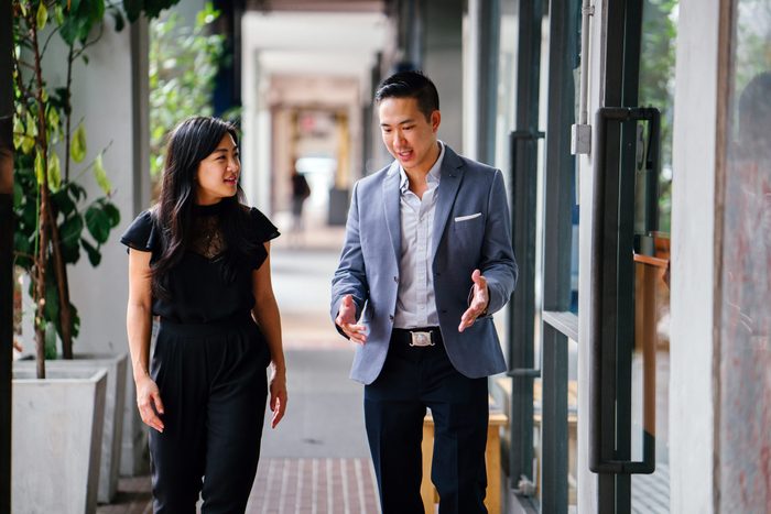 rude conversation habits - A portrait of two professional business people walking and talking. They are deep in conversation as they walk on a street in a city in Asia. The man and woman are both professionally dressed. 