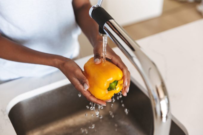 Close up of a afro american woman washing capsicum to make a salad at the kitchen