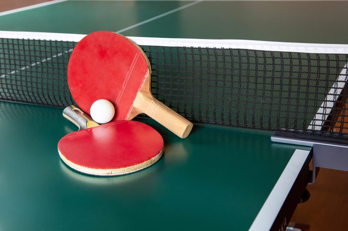 Two ping-pong rackets and a ball on a green table. Close-up, ping-pong net.