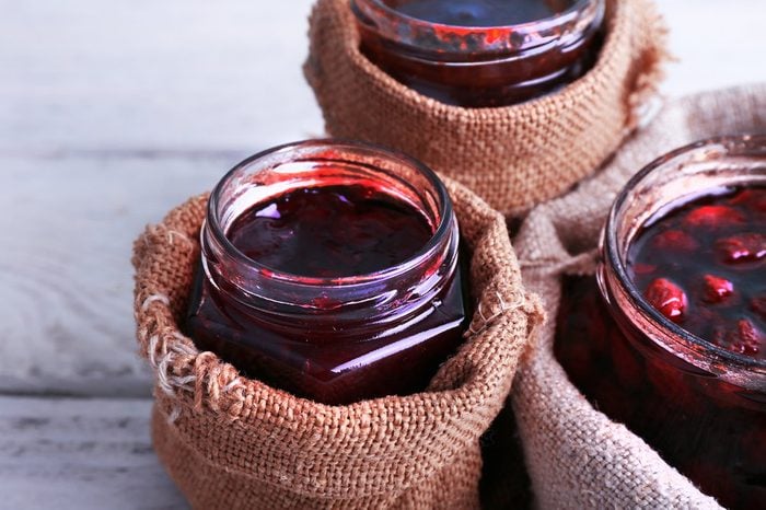 Homemade jars of fruits jam in burlap pouches on color wooden planks background