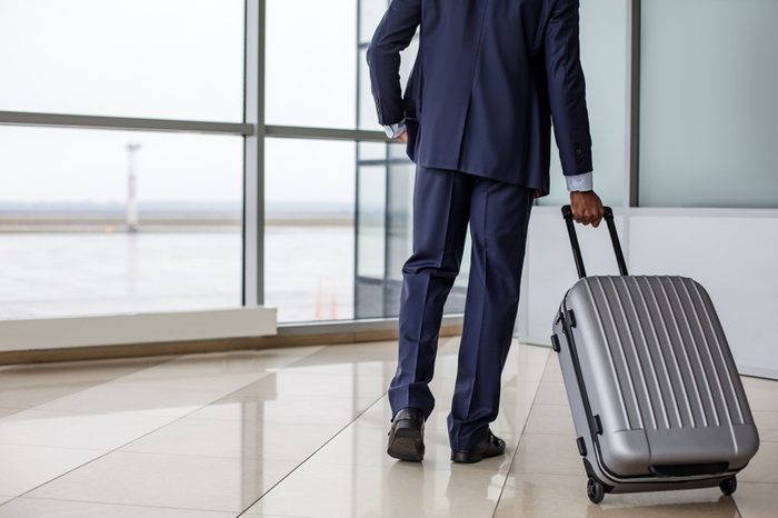 Travel concept. Back view of confident businessman in suit is walking along airport lounge while carrying his suitcase. Copy space in the left side