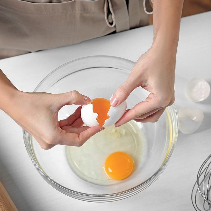 Woman cracking eggs into glass bowl