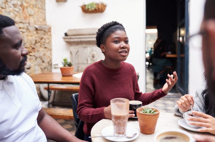 Young African woman talking with friends over coffee while sitting together around a table in the courtyard of a trendy cafe