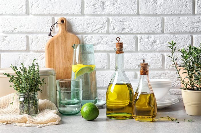 Fresh olive oil and kitchen utensils on table near brick wall