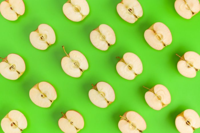 Fruit pattern on green background. Apple halves geometrical layout. Flat lay, top view. Food background.. Pop art design, creative summer concept.