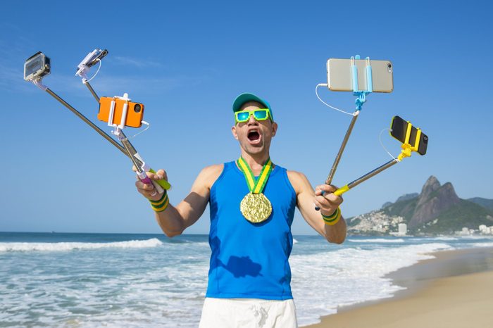 Gold medal athlete smiling for his many gadgets on selfie sticks as he poses for a picture on Ipanema Beach in Rio de Janeiro, Brazil