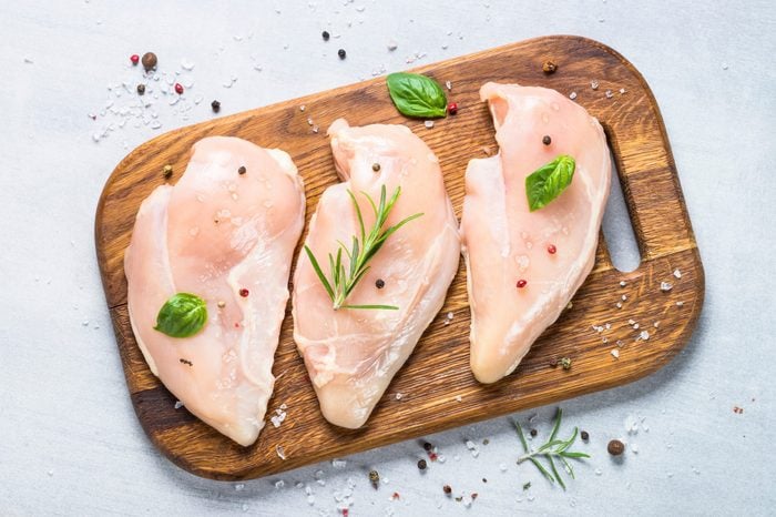 Raw chicken fillet with spices and herbs on cutting board. Light stone table top view.