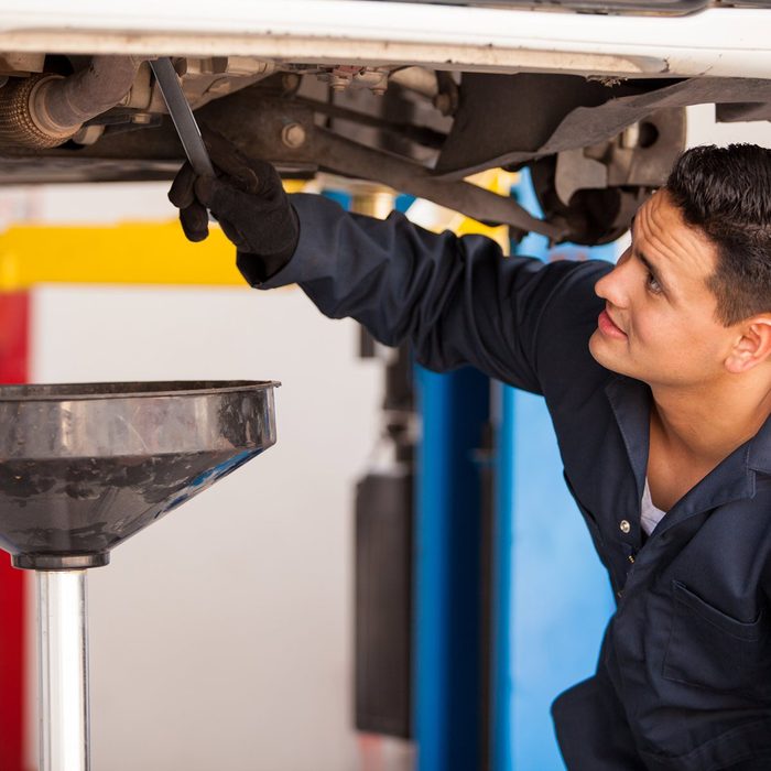 Young-Hispanic-mechanic-draining-engine-oil-from-a-car-for-an-oil-change-at-an-auto-shop