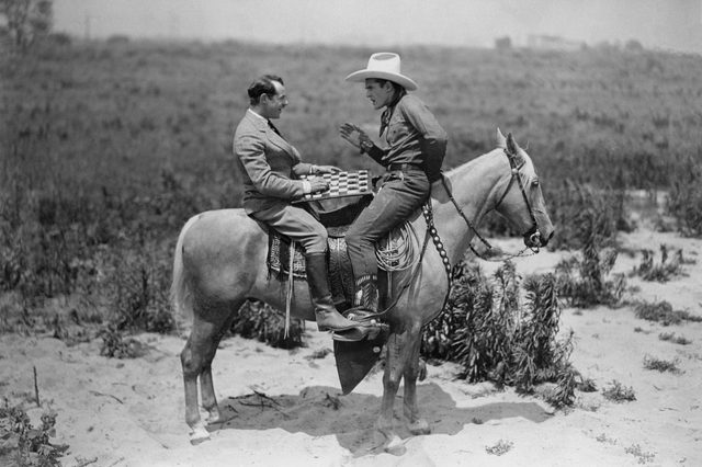 Cowboy and businessman playing checkers on horseback