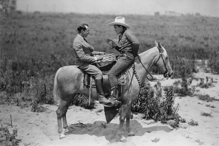 Cowboy and businessman playing checkers on horseback
