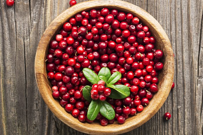 Ripe northern lingonberry in a wooden bowl on a background with twigs and leaves. Top View