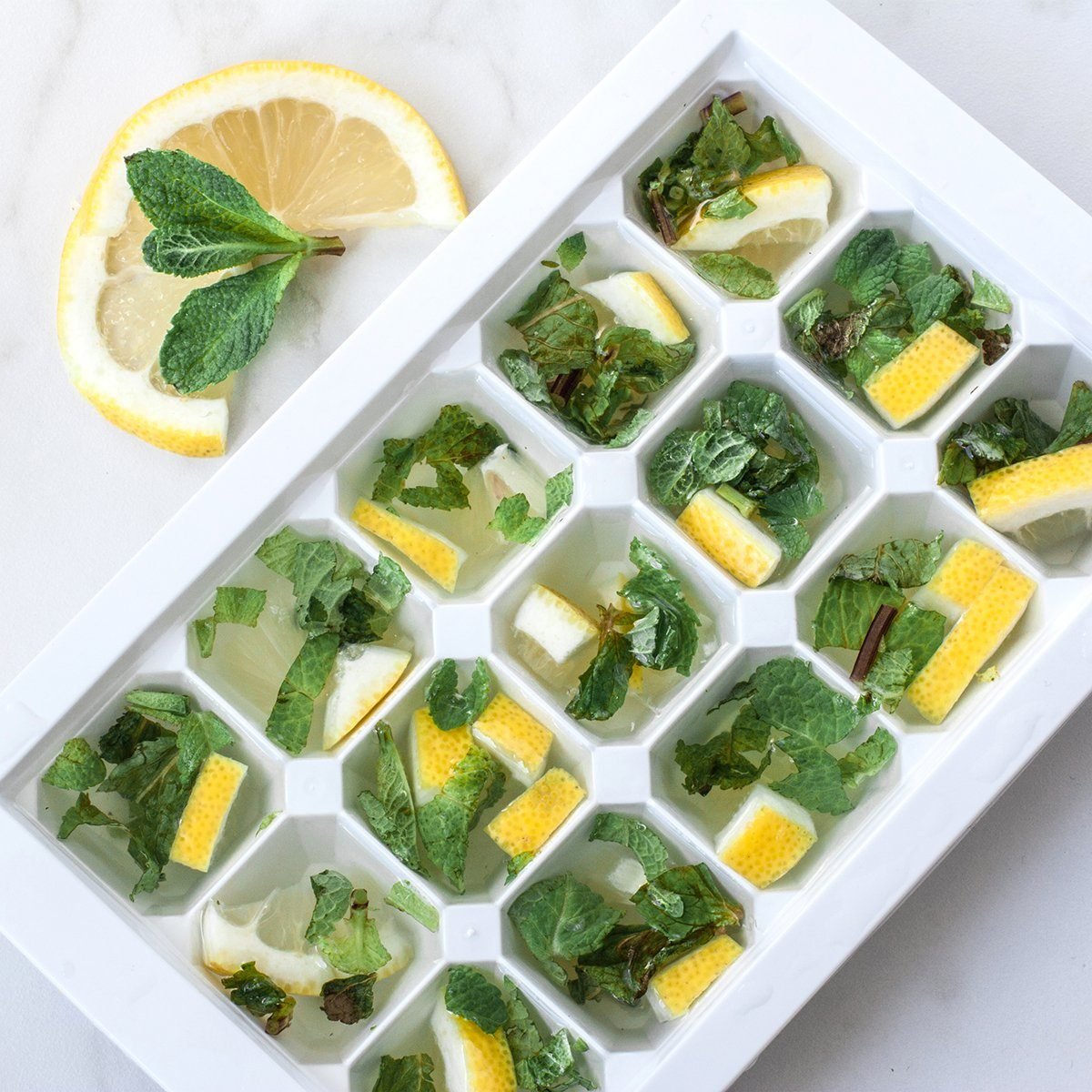 Cooking ice cubes with lemon and mint on marble background.