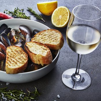 mussels in white wine sauce with glass of white wine white bread toasts