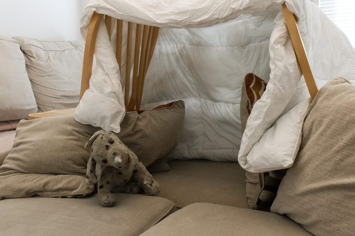 A pillow fort made of blankets chairs with a stuffed animal in the living room. Great for kids watching movies