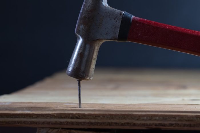 The carpenter uses a hammer to hit the nail on the wooden floor.