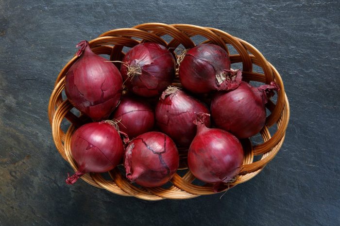 Red onions in wicker basket on slate table top