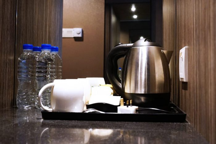 Coffee making set in a hotel room with stainless steel electric kettle, clean cup, teaspoon and bottle of water.