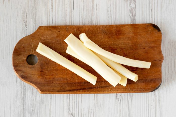 Top view, string cheese on rustic wooden board over white wooden background, top view. Healthy snack. Copy space.