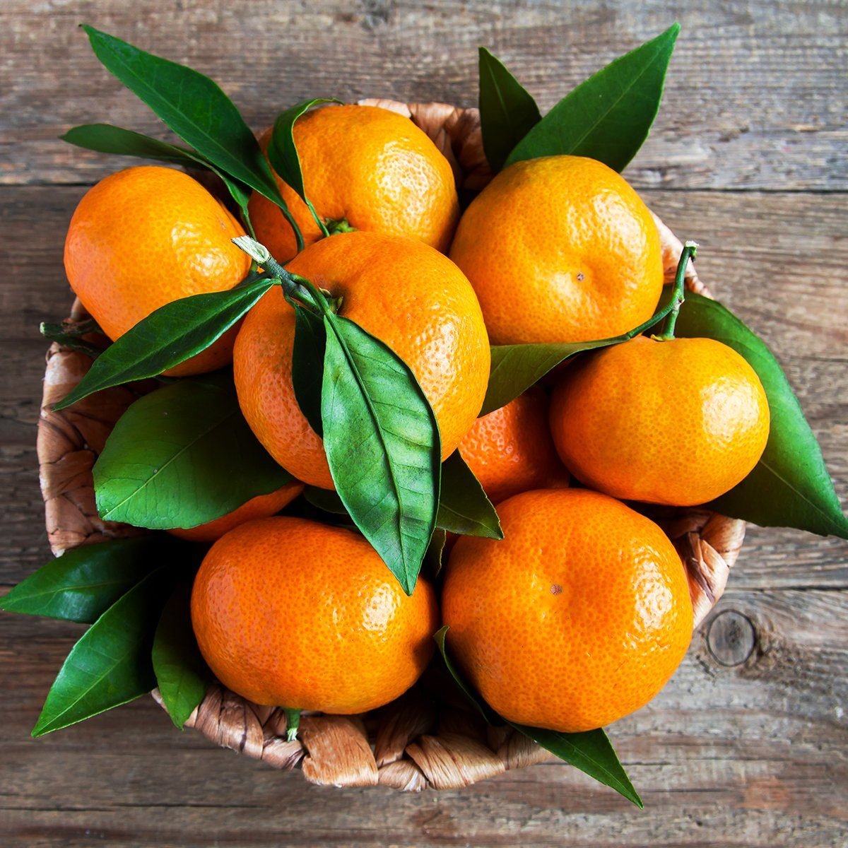 Tangerines (oranges, mandarins, clementines, citrus fruits) with leaves in basket over rustic wooden background